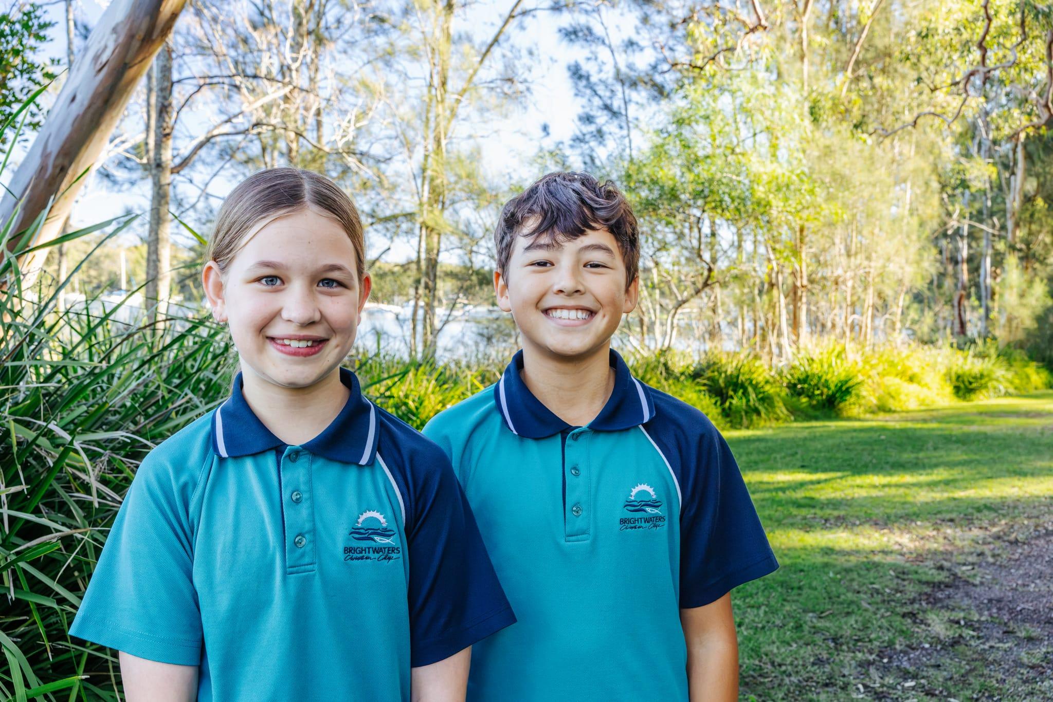 Two smiling Brightwaters Christian College students in uniform beside the lake