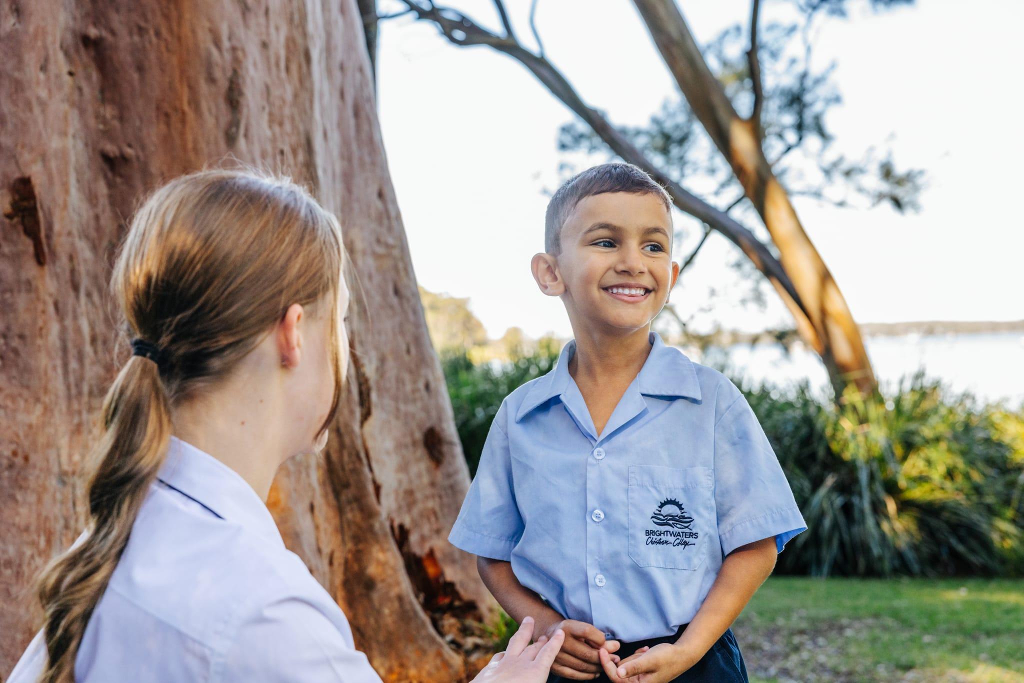 Pre-Kinder boy smiling with an older student buddy under gum trees beside Lake Macquarie