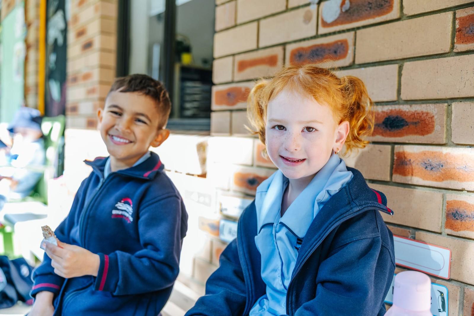 Two Pre-Kinder students enjoying a snack together outside their classroom near Morisset NSW