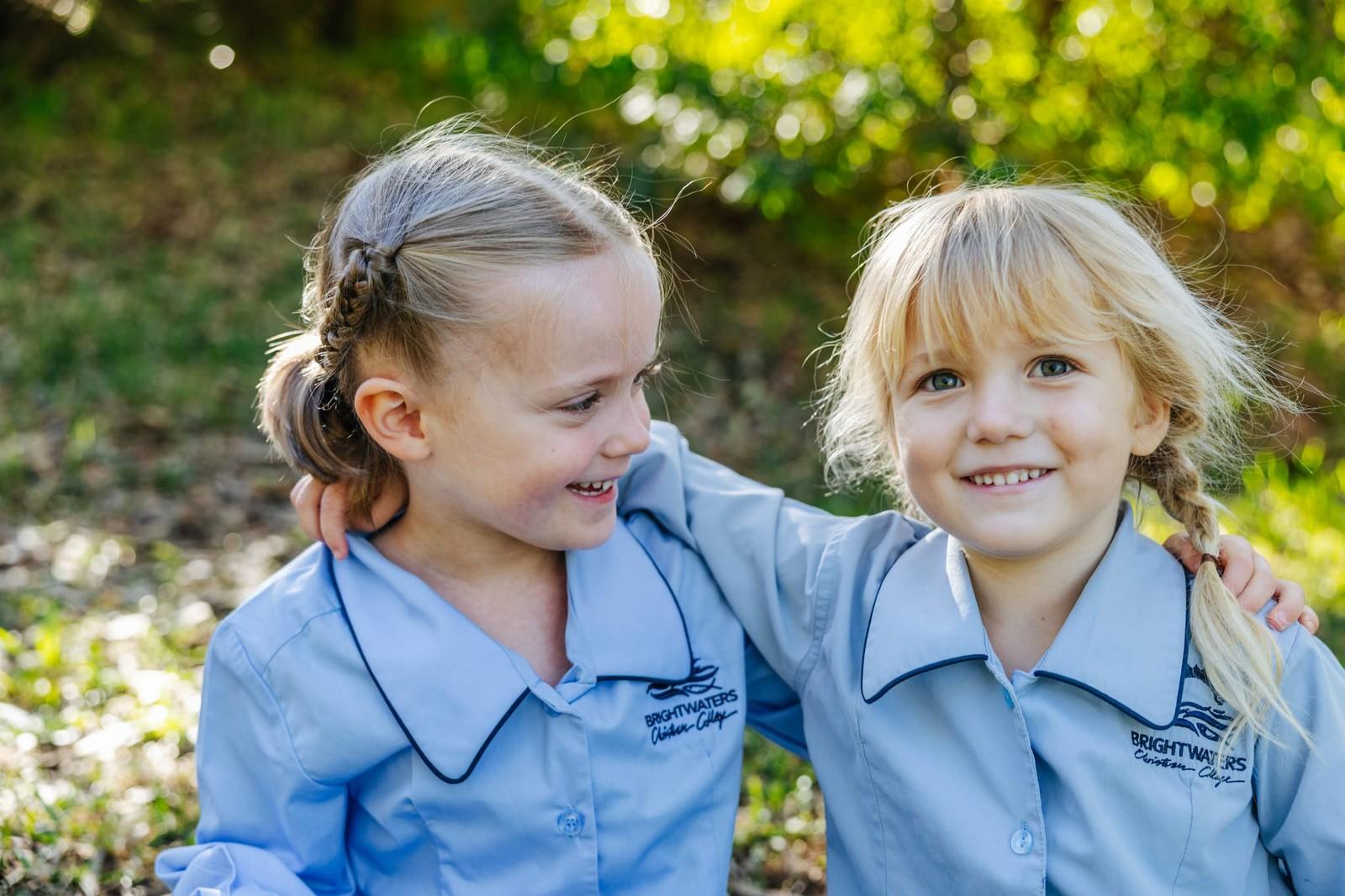 Two primary girls in school uniform sharing a smile outdoors on Lake Macquarie