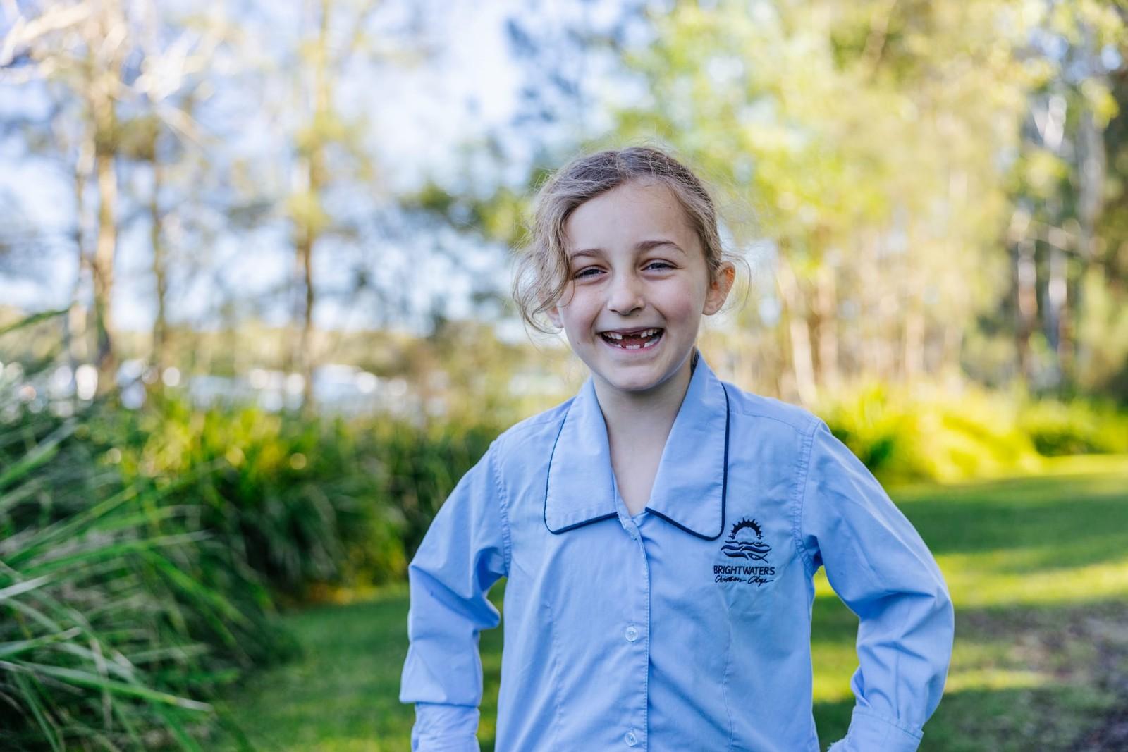 Laughing primary student in Brightwaters Christian College uniform in the leafy school grounds.