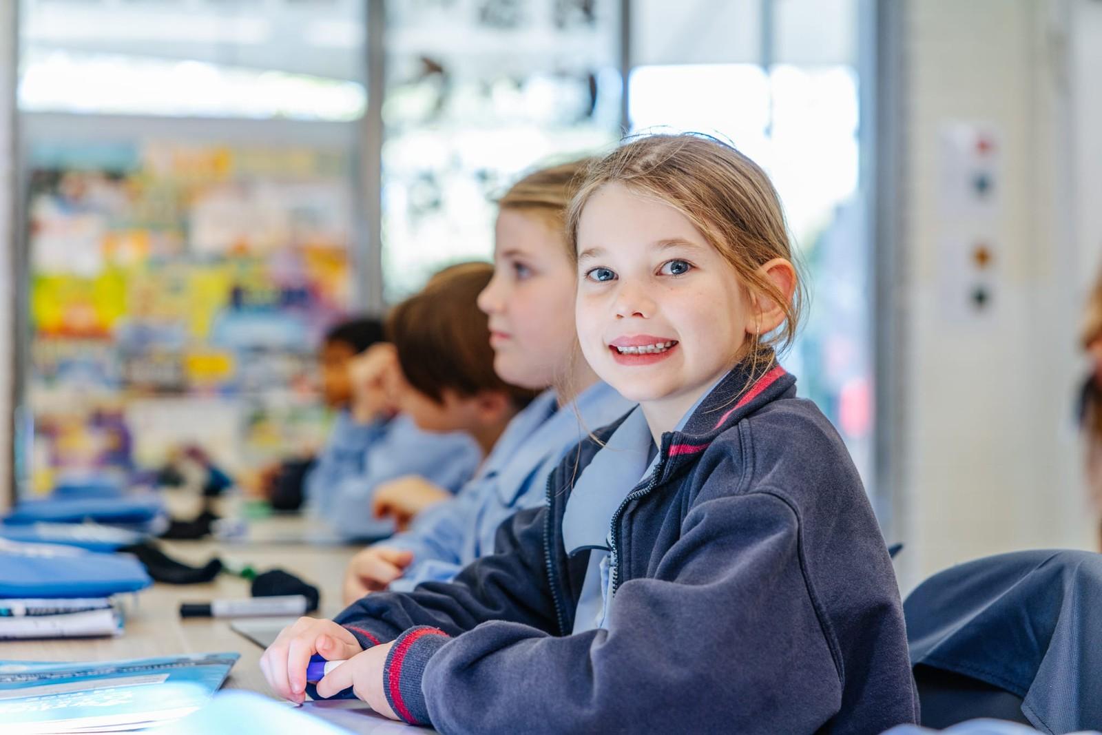 Smiling primary student seated with classmates in a Lake Macquarie Christian school classroom