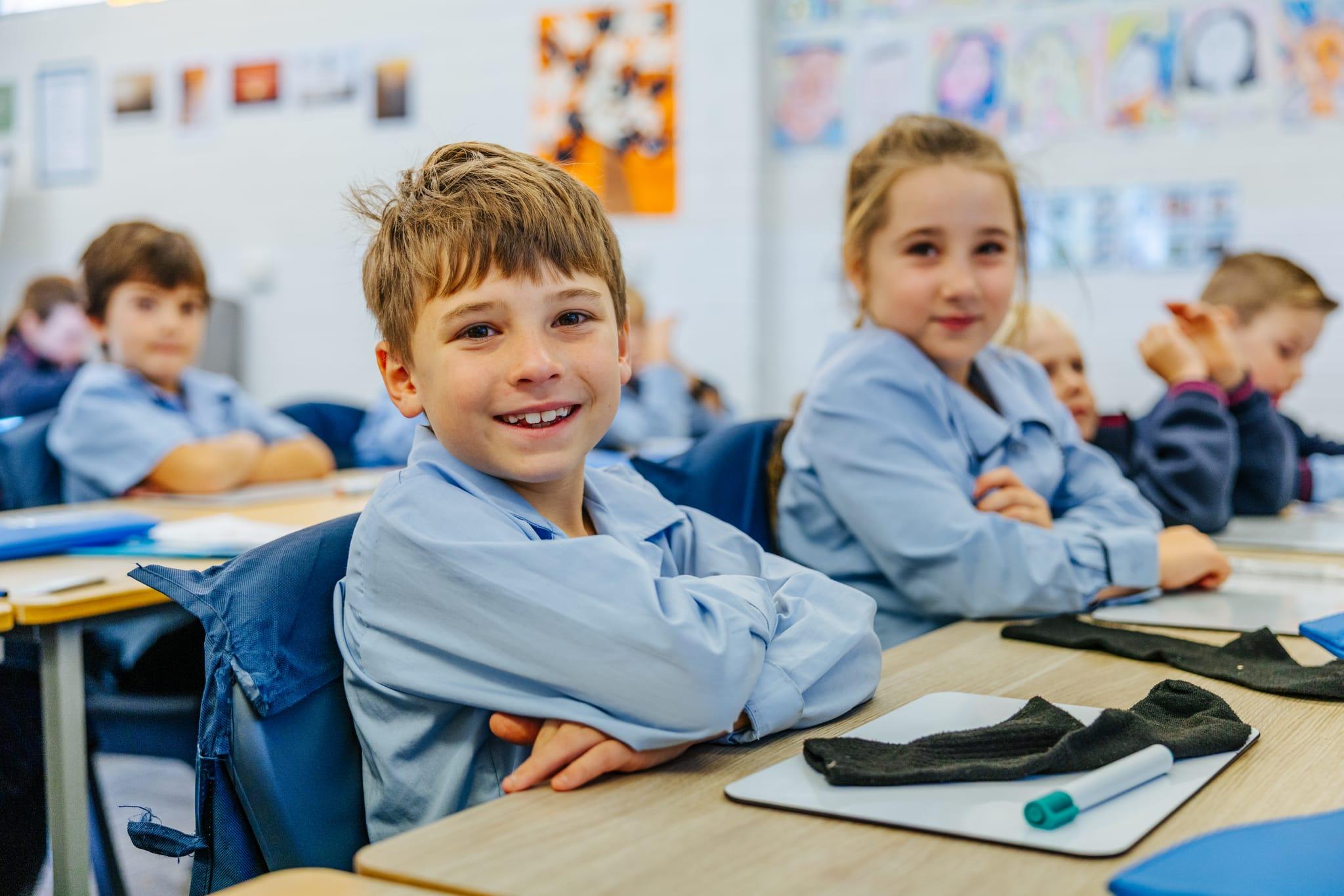 Primary students smiling at their desks in a bright classroom