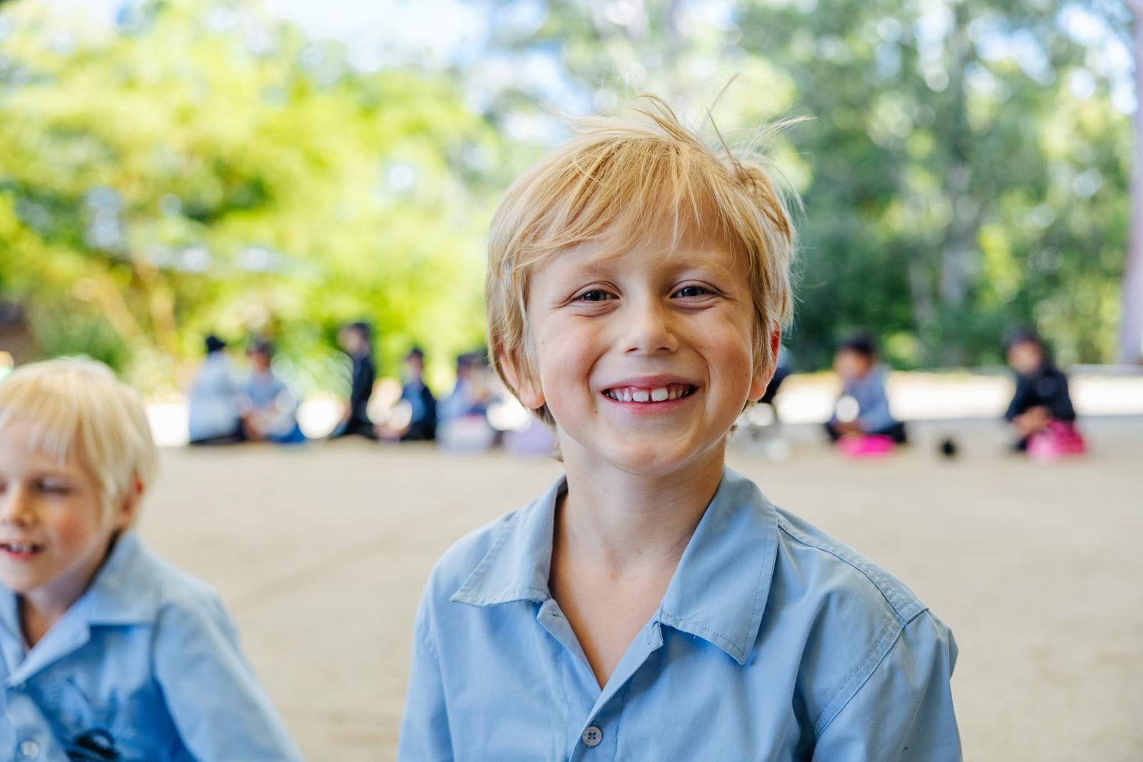 Smiling primary student outdoors with classmates gathered in the background