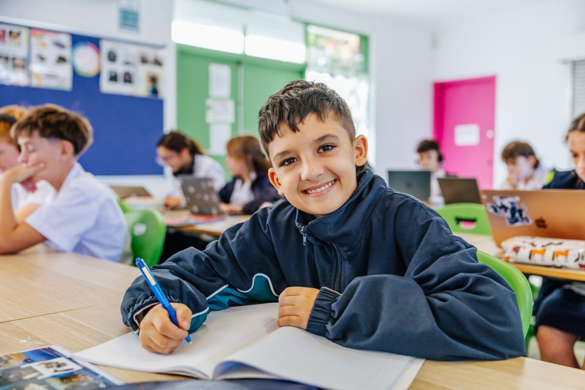 Smiling student writing in his workbook in a classroom at Brightwaters Christian College