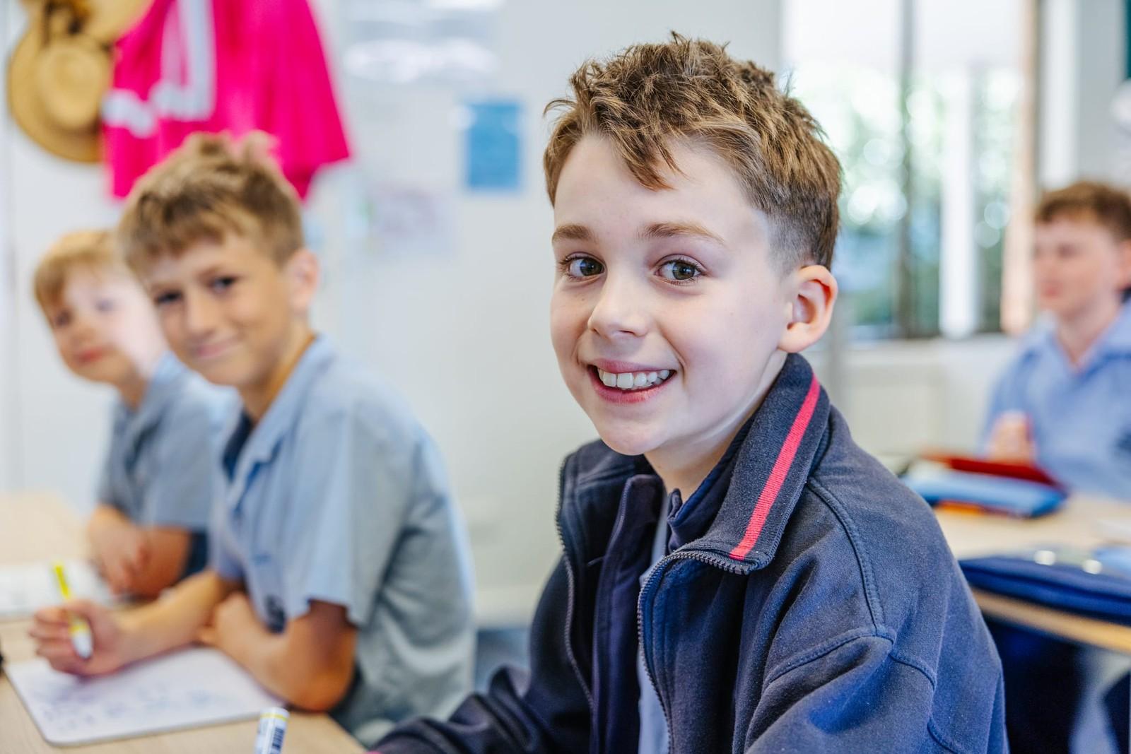Smiling primary student at his desk with classmates in a Brightwaters classroom