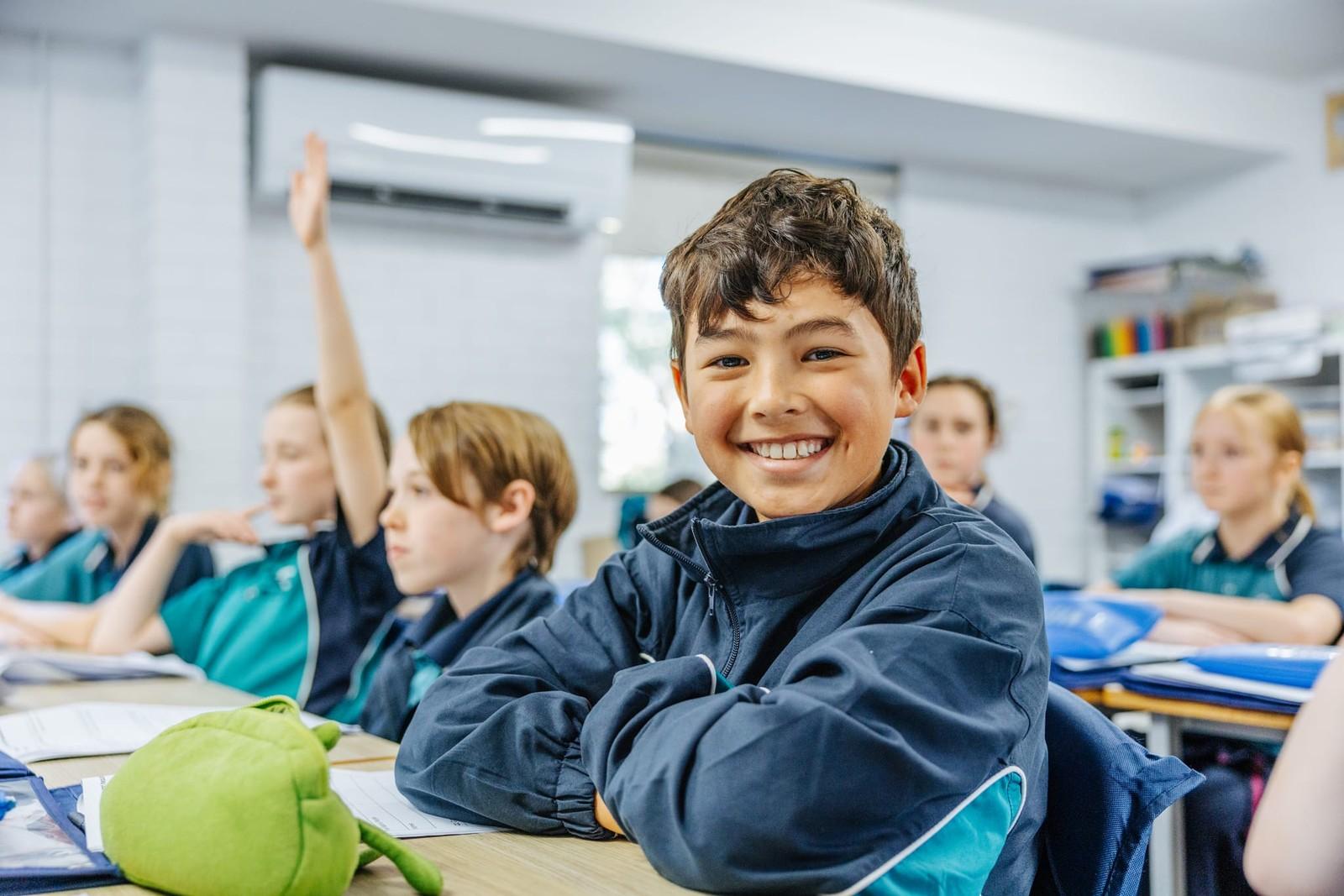Smiling student in class while a classmate raises their hand at our Lake Macquarie school.