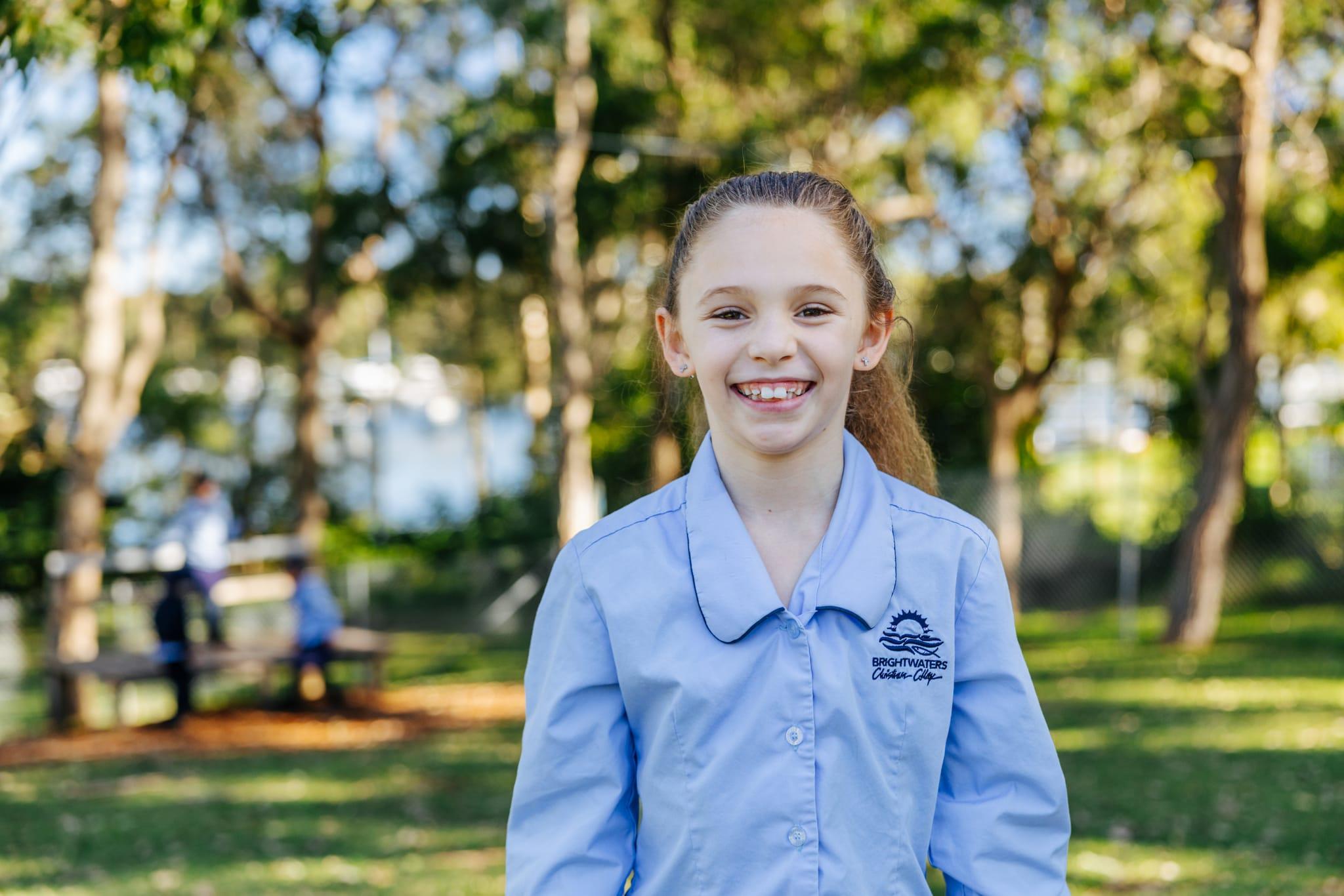 Smiling primary student in school uniform outdoors among the trees near Morisset NSW