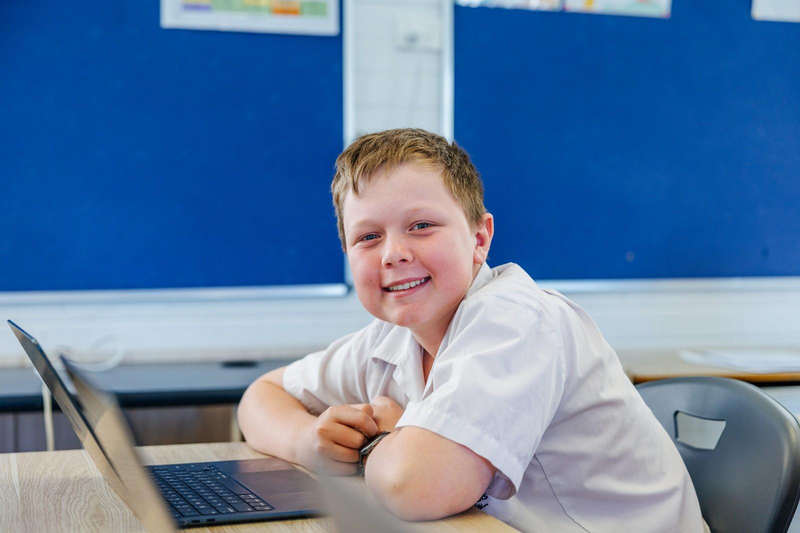 Smiling secondary student with a laptop in class, looking ahead to future study pathways