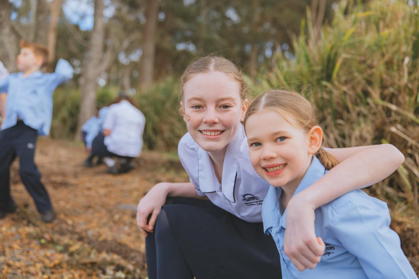 Older student with her arm around a younger student during outdoor learning in bushland near Morisset NSW