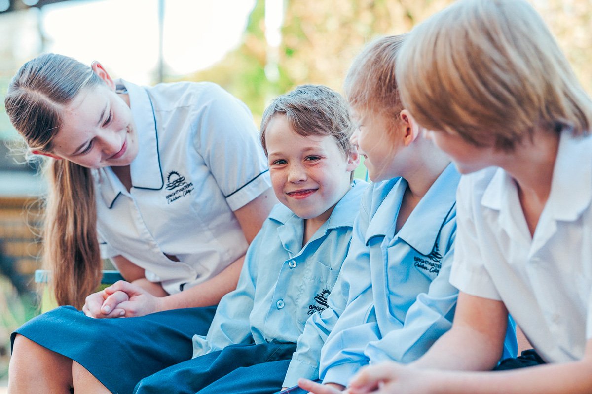 Kindergarten students sitting on sitting on bench surrounded by supportive friends