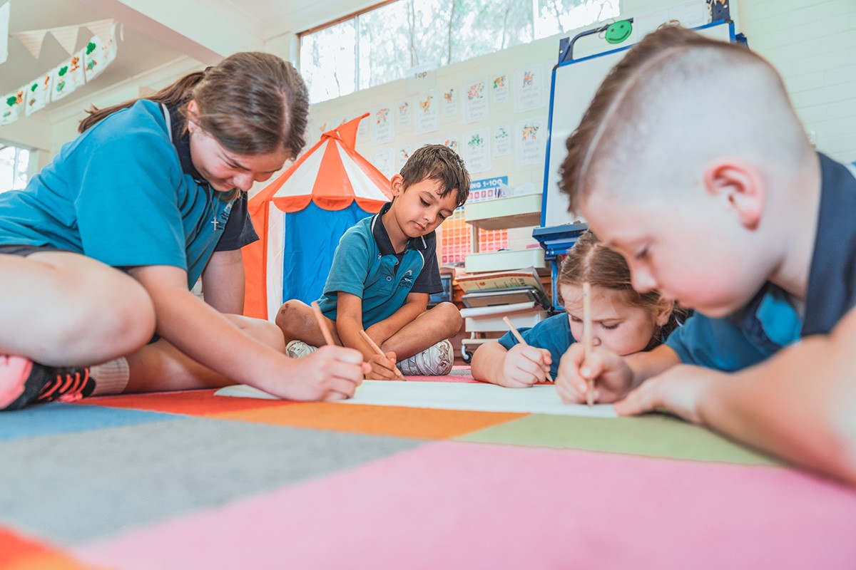 group of young primary schools students sitting on the floor daring on sheet with pencils