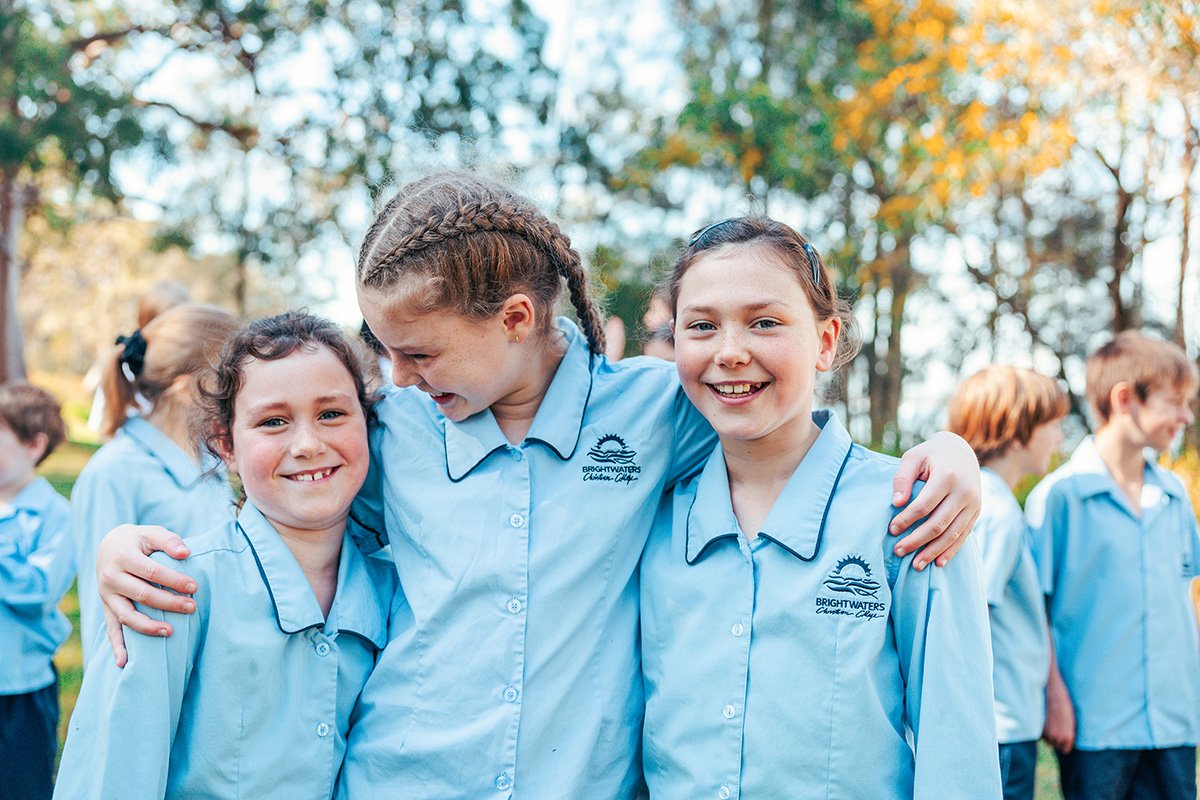 Three different female primary school students who are outside, hugging, and smiling