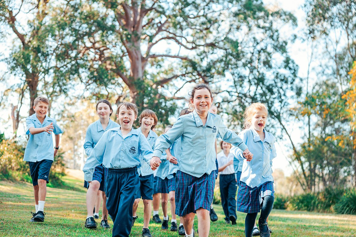 Group of girls and boys in uniform holding hands running outside on grass