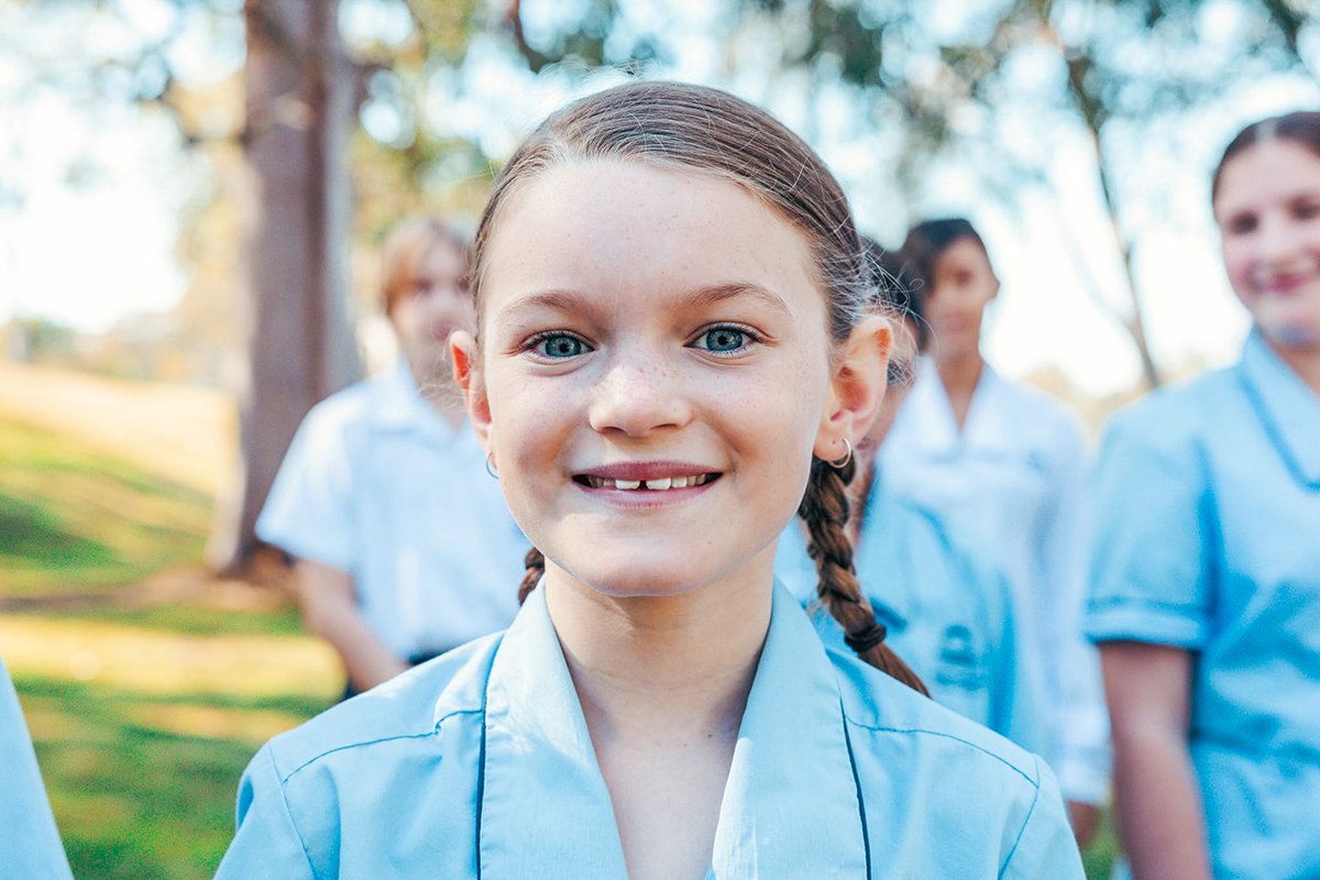 Close-up of smiling primary school student enrolled at Brightwaters Christian College with classmates in the background